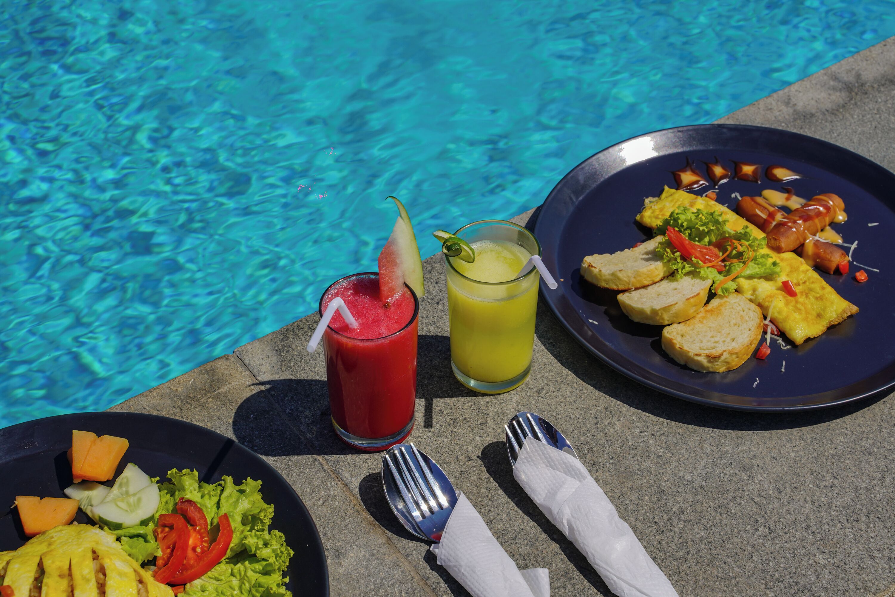 Ein Tisch mit Essen, zwei Getränken und einem Pool im Hintergrund.