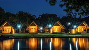 A row of wooden cabins with warm lighting, a reflective water body in the foreground, and a dark sky. - Sofanda Resort (Nangamiro)
