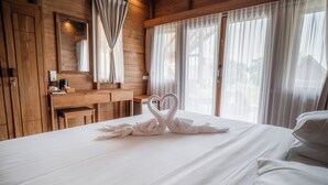 A hotel room with a wooden interior, a bed with white linens, a bedside table with a lamp, and a large window with sheer curtains. - Sofanda Resort (Nangamiro)