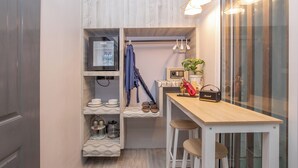 Eine kleine Küche mit Holztisch, Barhocker, einer Kleiderstange und einem kleinen Kühlschrank.