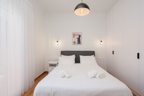 Un lit bien fait, avec du linge de lit blanc et deux serviettes, une table de chevet avec une lampe et un tableau accroché au mur.