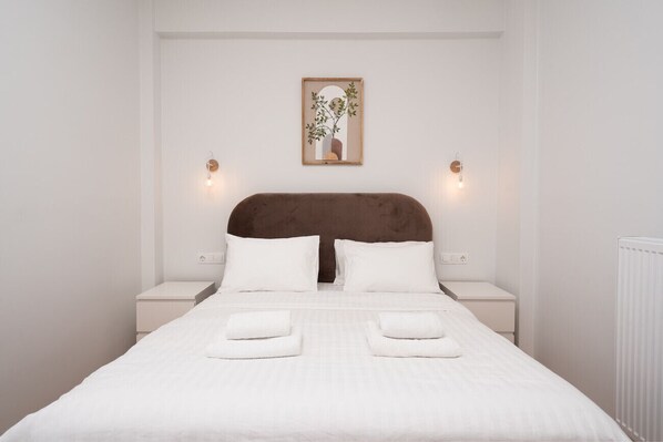 A neatly made bed with white linens and two pillows, a brown headboard, and two bedside tables with lamps.