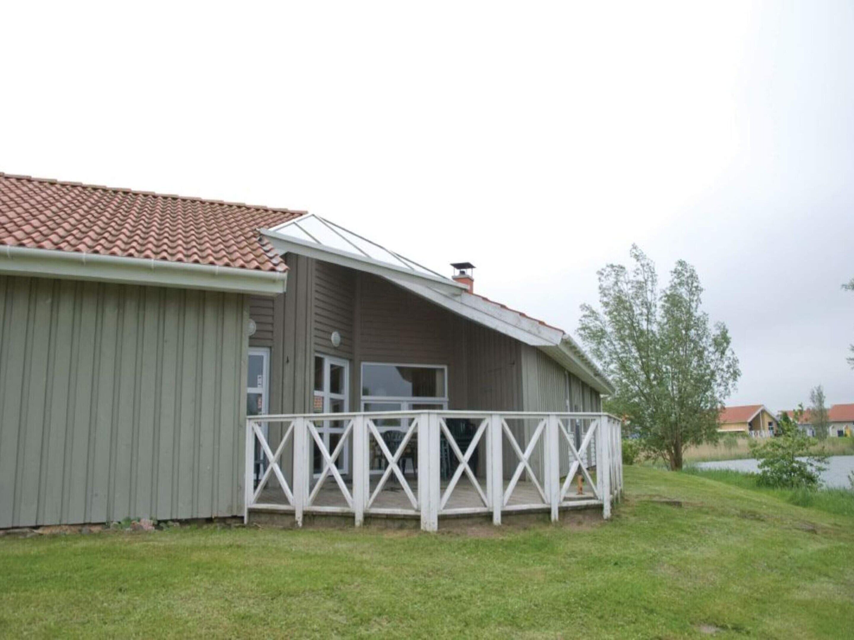 Ein einstöckiges Gebäude mit rotem Ziegeldach, einer weißen Veranda mit Querstreben und einem kleinen Fenster.
