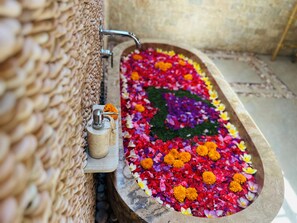 Une baignoire en pierre remplie de p étales de fleurs aux couleurs vives, un mur de pierre et un robinet en métal.