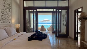 A bedroom with a large bed, a view of the beach, and a sliding glass door leading to a balcony.