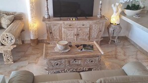 A living room with a large flat-screen TV, a beige sofa, a coffee table, and decorative items including a lamp and a vase.