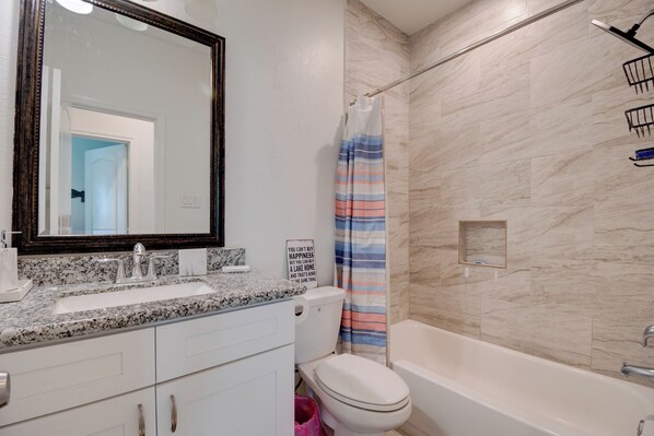 Een badkamer met een wastafel met granieten blad, een wit toilet, een bad en een douchegordijn.