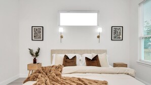 Une chambre avec un grand lit, deux tables de chevet, une commode, une fenêtre avec stores et deux lampes fixées au mur.