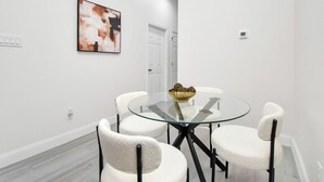 Un espace repas moderne avec une table en verre entourée de chaises blanches, un bol doré posé sur la table et un tableau accroché au mur.