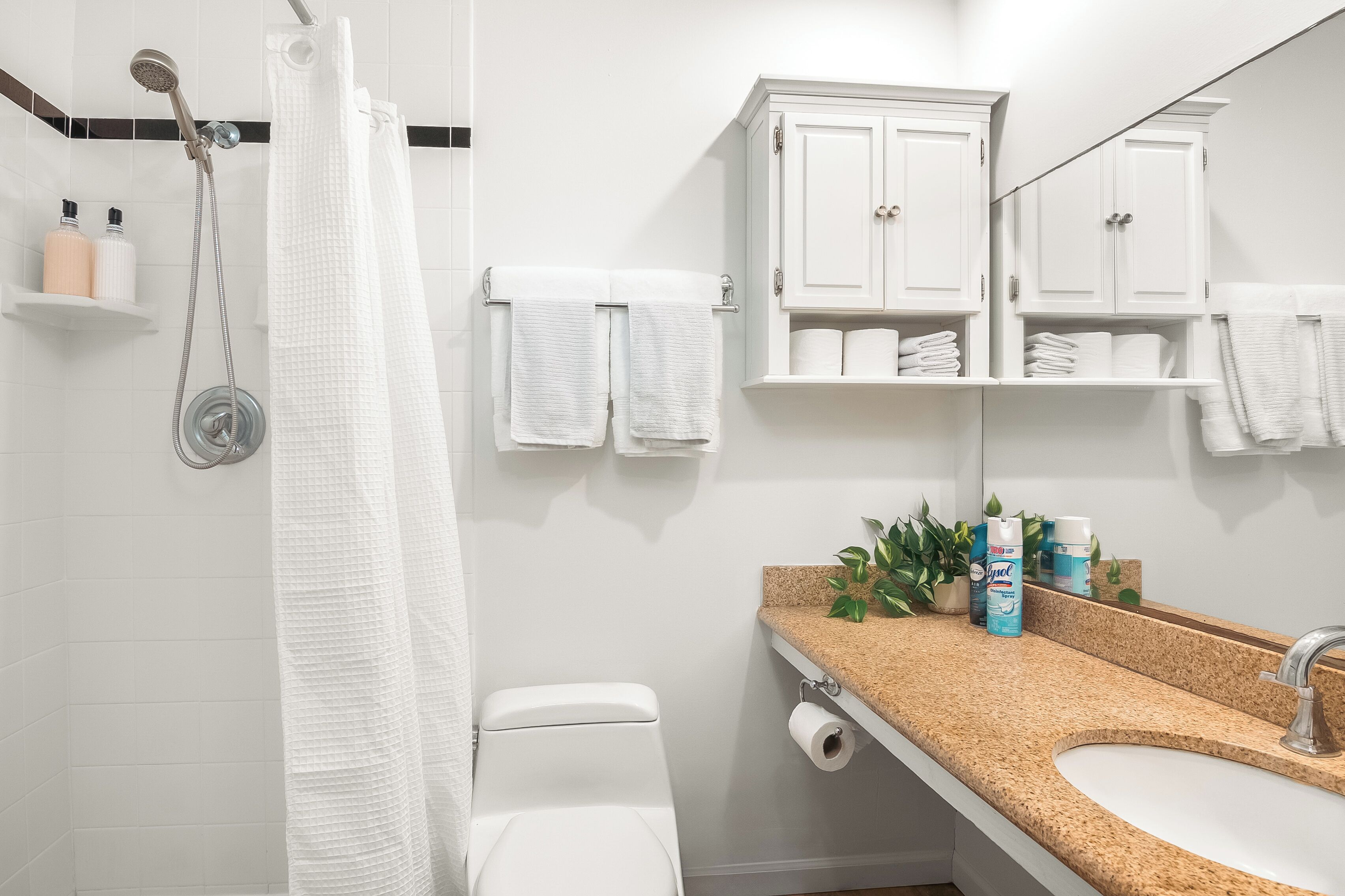 A modern bathroom with a shower, toilet, and sink. There are white cabinets above the sink and a towel rack with towels.
