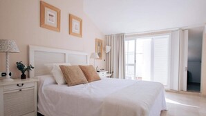 A large bed with white bedding and two decorative pillows, a bedside table with a lamp, and a window with curtains. - Creta sunset by BH Marbella (Marbella)
