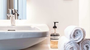 A bathroom with a white sink, a mirror, a towel dispenser, and a wall socket. - Charming Studio Retreat for Two in Central Ghent (Gent)