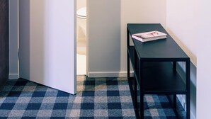 Ein Korridor mit Schachbrettmuster-Boden, einer weißen Tür, einem schwarzen Tisch mit einer Zeitschrift und einem Holzaufhänger an einem schwarzen Regal.