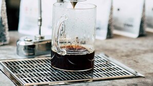 Eine Kaffeemaschine, die Espresso in ein Glas auf einer Metallschale füllt.