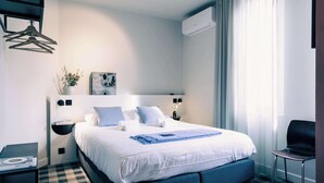 Ein Hotelzimmer mit einem großen Bett, einem Nachttisch, einem Sessel und einer Wandklimaanlage.