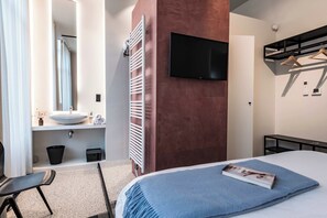 A modern hotel room with a large bed, a flat-screen TV mounted on the wall, a built-in sink, and a towel rack.