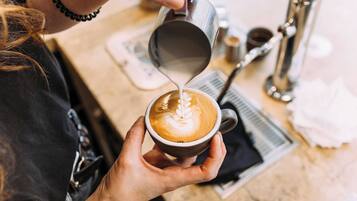A person pouring milk into a cup of coffee, creating a latte art design.