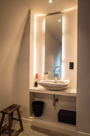 A modern bathroom with a white sink, a mirror, and a small stool.