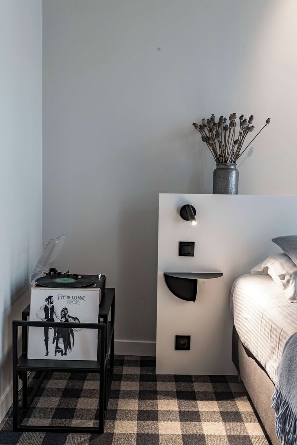 A bedroom with a bed, a dresser with a vase of dried flowers, a record player, and a wall-mounted light fixture. - Studio for 2 in City of Ghent (Gent)