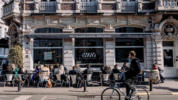 A cafe named "Way Specialty Coffee - Bake House" with outdoor seating and a cyclist passing by. - Studio for 2 in City of Ghent (Gent)