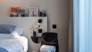 Et pænt opredt værelse med en seng, en stol, et lille bord og en reol med bøger samt et skilt.
