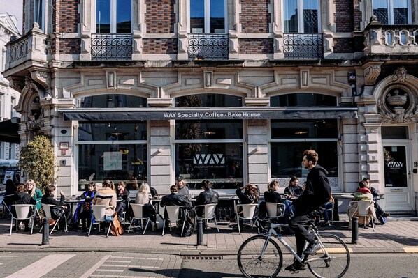 A cafe named "Way Specialty Coffee - Bake House" with outdoor seating and a cyclist passing by. - Studio for 2 in City of Ghent (Gent)