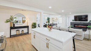 Un salón moderno con una isla blanca, una chimenea y un televisor montado en la pared.