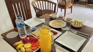 A breakfast table with plates of fruit, a jug of juice, and various breakfast items. - Easy Stay (Kandy)