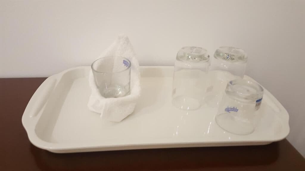 Una bandeja blanca con cuatro vasos pequeños y un paño.