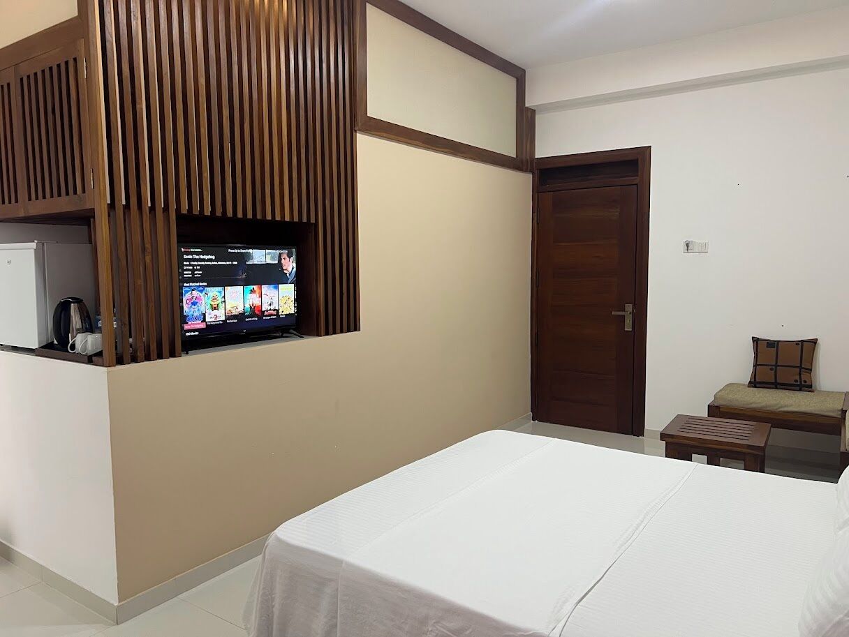 Habitación de hotel con cama, una mesita, un televisor montado en un panel de madera y una puerta.