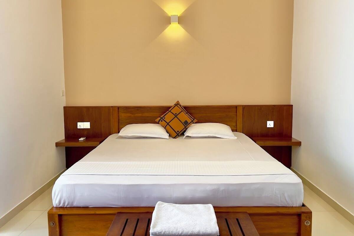A neatly made bed with a wooden headboard, two bedside tables, and a wall-mounted light fixture.