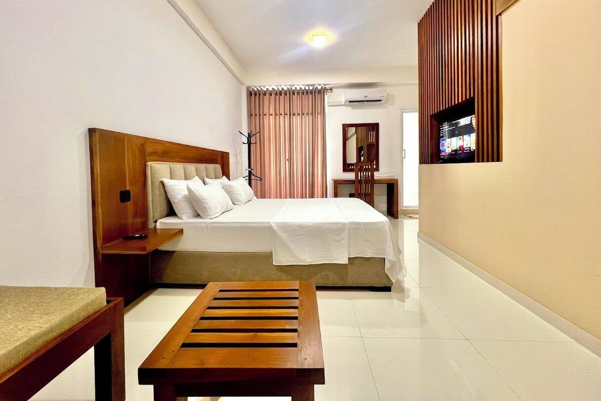 A hotel room with a bed, bedside table, and a wooden bench.