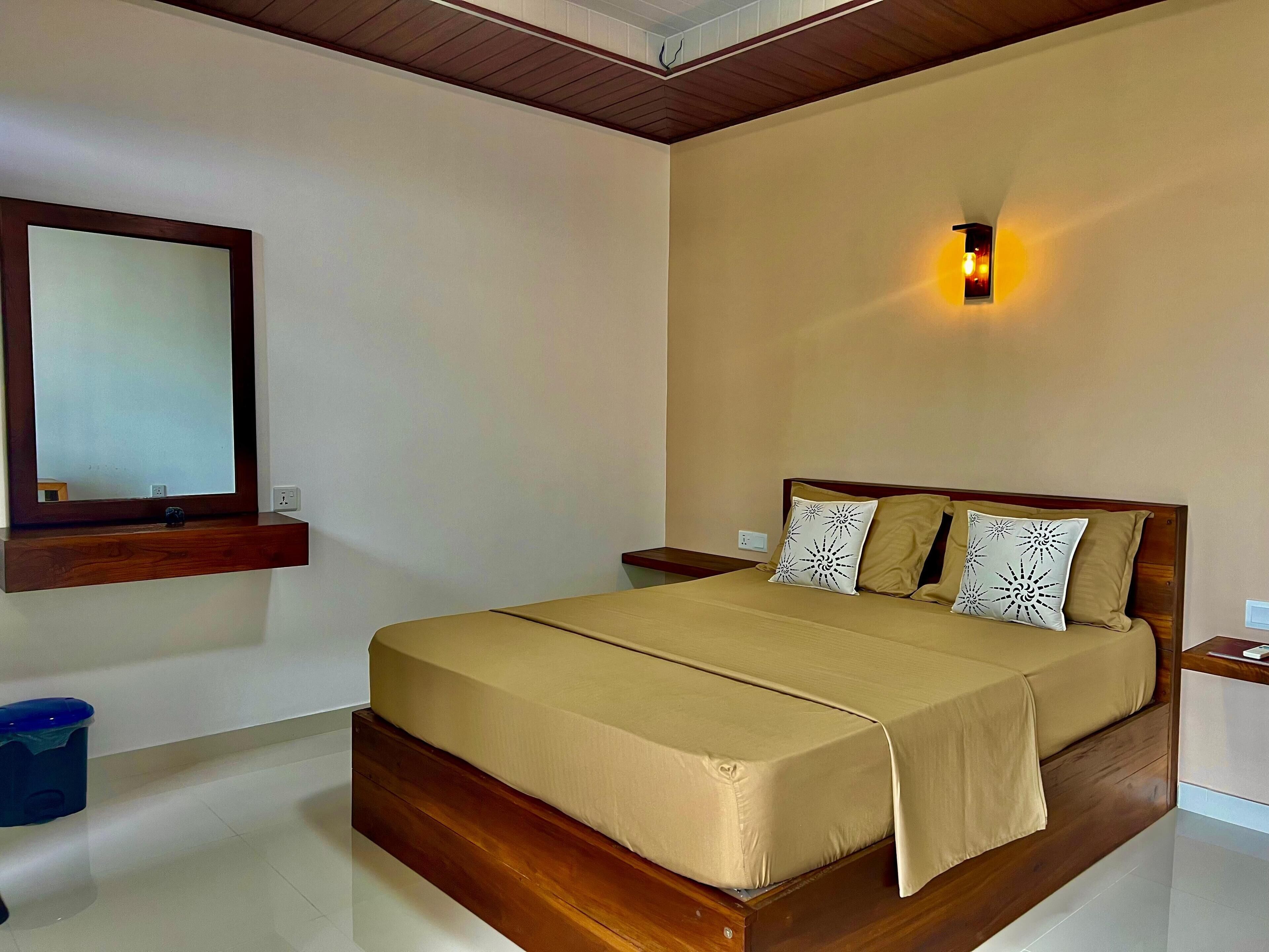 A bedroom with a wooden bed, a bedside table, a nightstand, a wall-mounted light, and a mirror.