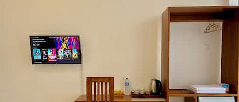 A small, neatly organized room with a wooden desk, a chair, a television mounted on the wall, a mini-fridge, and a wooden cabinet with a hanger.