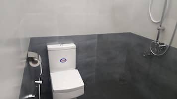 A bathroom with a toilet, a shower, and a wall-mounted toilet paper dispenser.