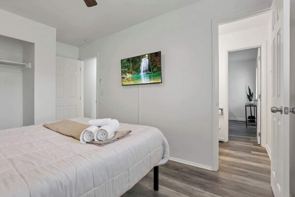 Un dormitorio moderno con una cama grande, un televisor de pantalla plana en la pared y vistas a un pasillo que conduce a otra habitación.