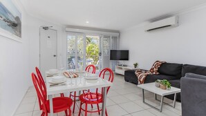 Een moderne woonkamer met een witte eettafel, rode stoelen, een grijze bank en een flatscreen televisie.