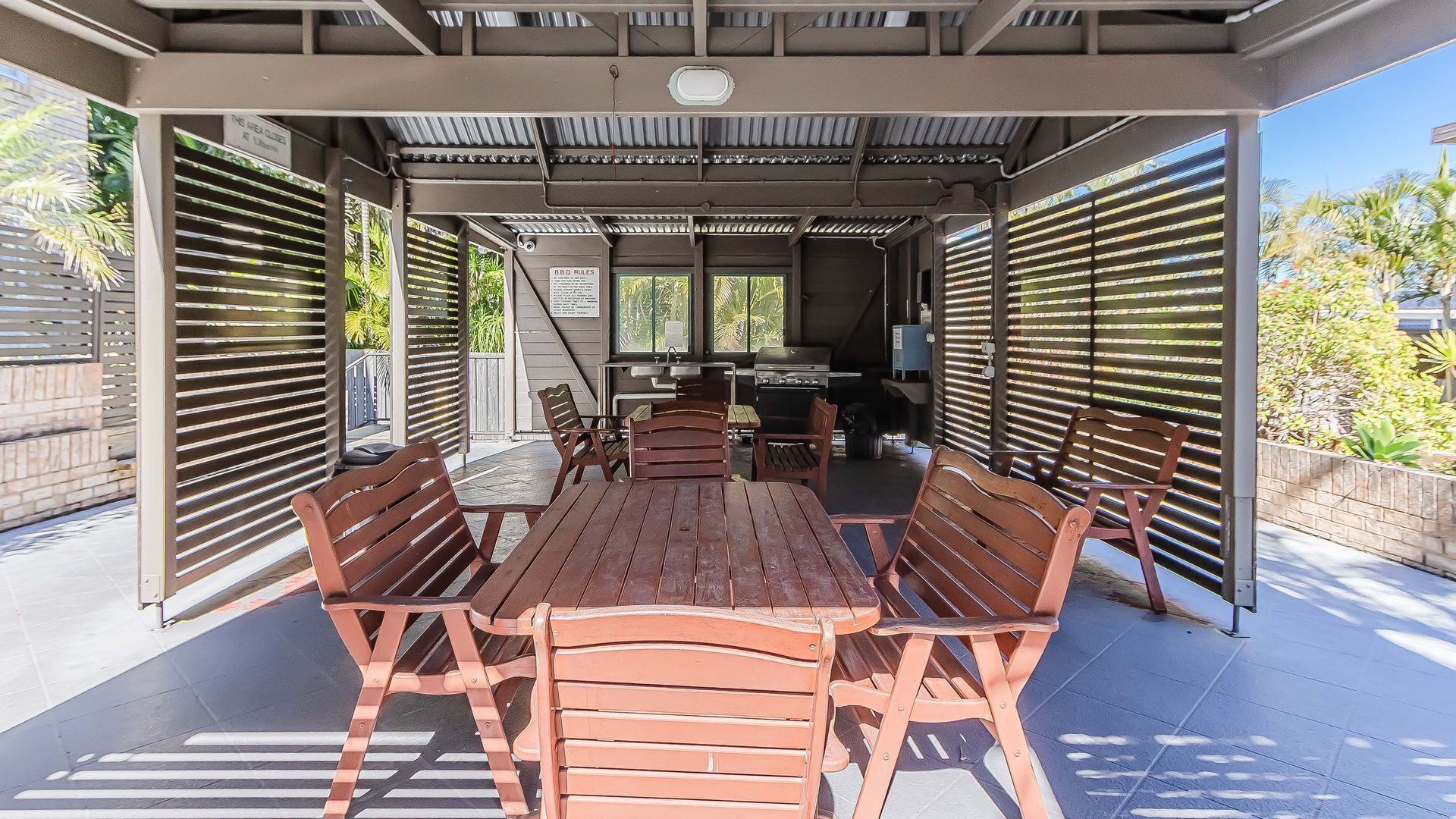 Een terras buiten met een overdekte zithoek, een barbecue en uitzicht op de groene omgeving.