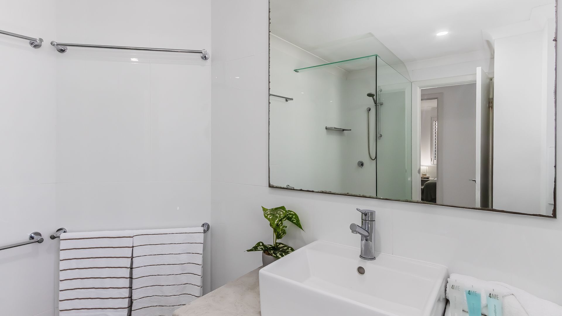 Une salle de bain moderne avec une douche à parois de verre, un grand miroir, un lavabo blanc et une serviette à rayures.