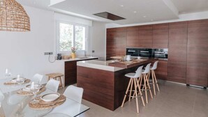 Une cuisine moderne dotée d’un îlot central, de meubles en bois et d’un coin repas avec une table en verre et des chaises blanches.