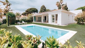 Une maison moderne dotée d’une piscine, entourée d’une végétation luxuriante et de palmiers.