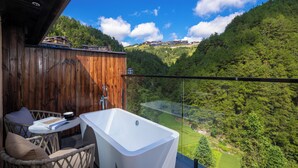 Un balcone con una vasca da bagno bianca, mobili in vimini e vista su una valle boscosa.