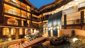 Un hotel a più piani con balconi, una cascata decorativa e un giardino con scalini e piante.