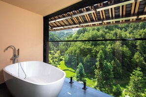 A modern bathroom with a freestanding bathtub, a glass shower enclosure, and a view of a lush forest through a large window. - Sanchunli Ji Garden Meisu (Qiandongnan)
