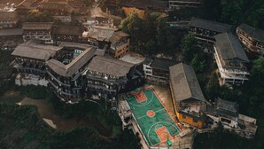 Vista aerea di un villaggio tradizionale con case a terrazze, un campo da basket e un fiume.