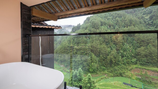 Un bagno moderno con una vasca da bagno ampia e vista su una rigogliosa foresta e campi a terrazza.