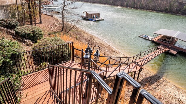 Une terrasse en bois avec des rampes en métal, donnant sur une rivière où naviguent des bateaux.