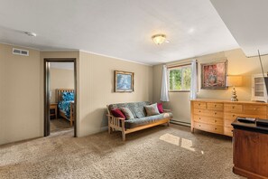 Een kamer met een bank, een houten kast, een schilderij en een raam met gordijnen.