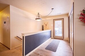 A hallway with a wooden floor, a dark-colored bench, a light fixture, a door with a view, and a small plant.
