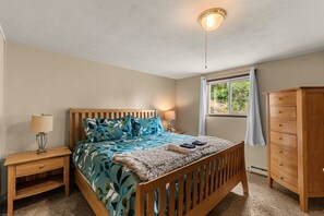 Een slaapkamer met een houten bed, nachtlampjes, een dressoir en een raam met gordijnen.